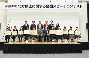 数名の大人と、賞状を持っている生徒が椅子に座っている集合写真